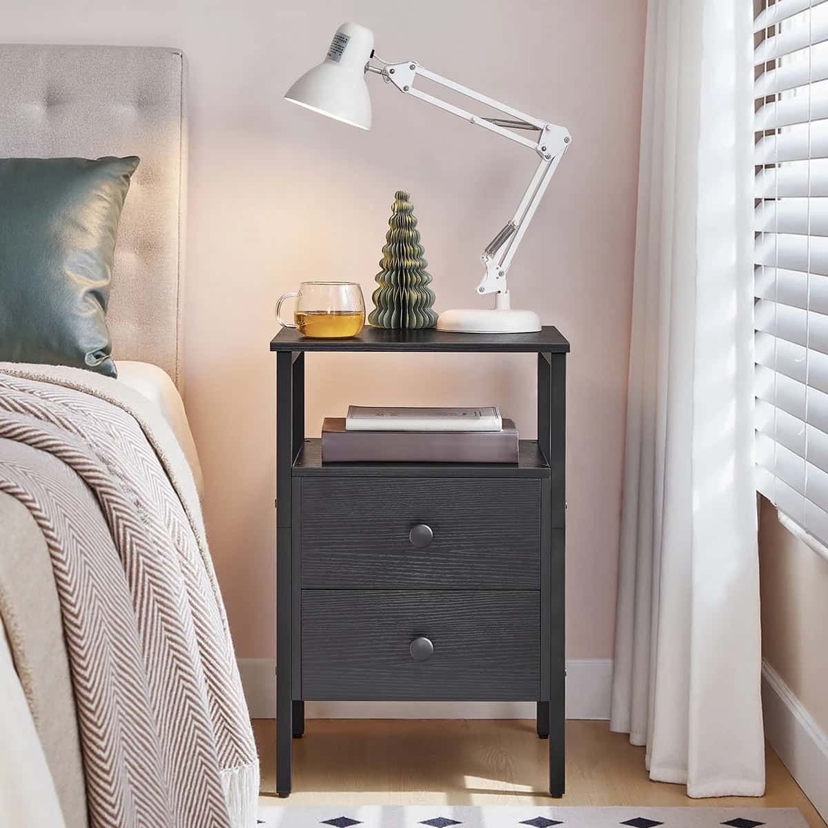 Black nightstand with a lamp, glass, and decorative item next to a bed.