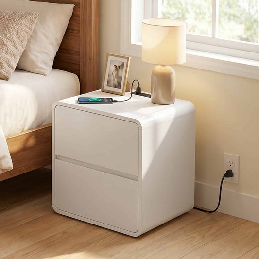 White nightstand with lamp and phone on a wooden floor next to a bed.