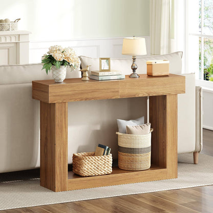 A light oak wood console table styled in a bright living room next to a cream sofa, decorated with a vase of white flowers, a table lamp, and storage baskets underneath.