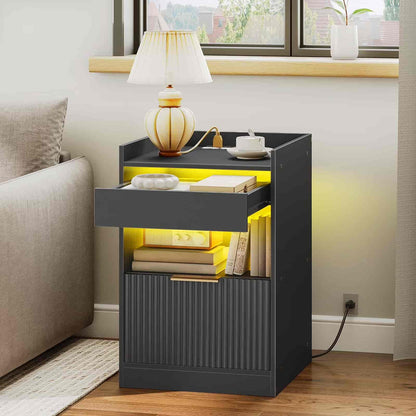 Black side table with glowing yellow interior, lamp, books, and cup in a living room setting.