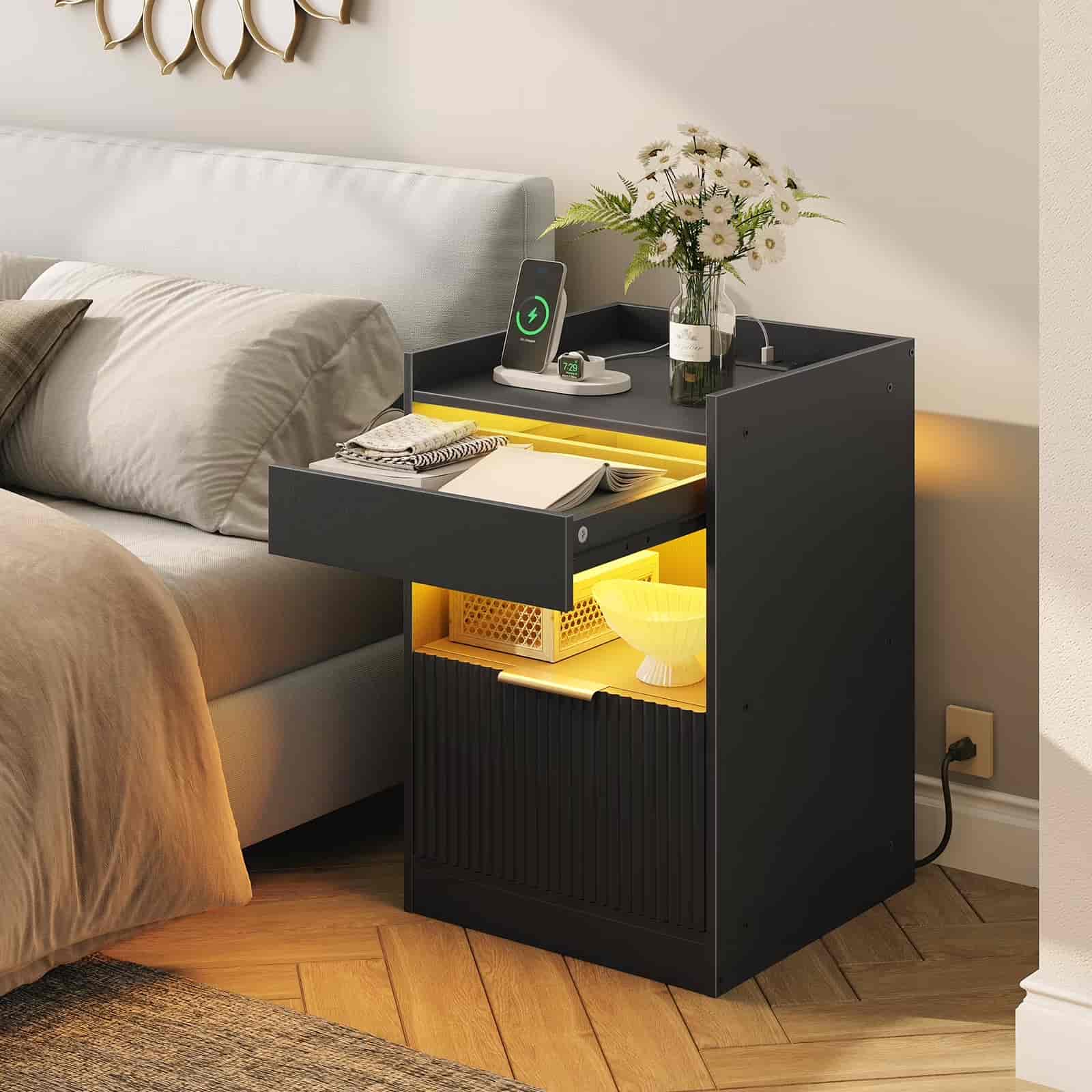 Black nightstand with yellow illuminated drawer next to a bed