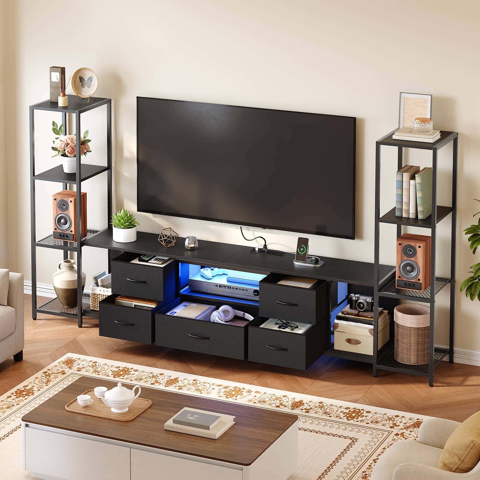 A modern black media console with built-in drawers and open shelving, styled in a living room setting with a TV, side shelves, and a coffee table.
