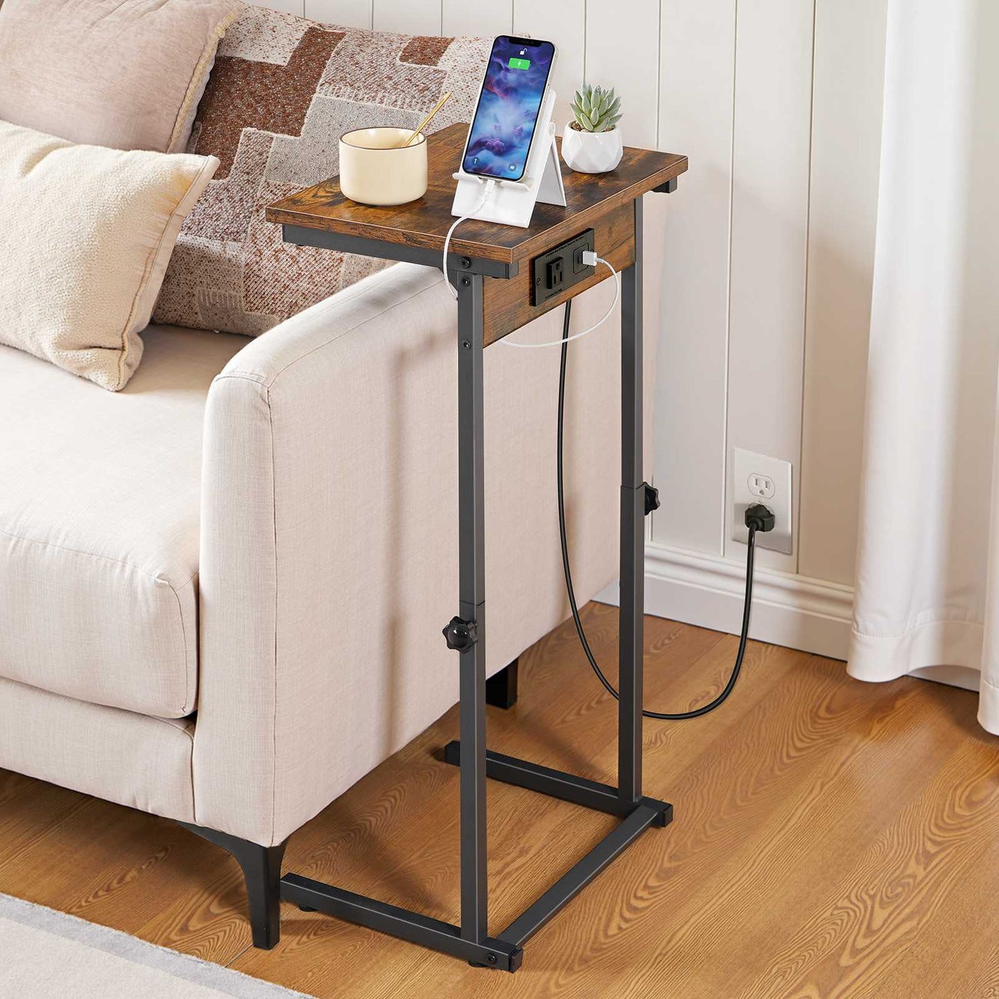 Rustic brown C table sliding under a white sofa armrest charging a tablet and a smartphone.