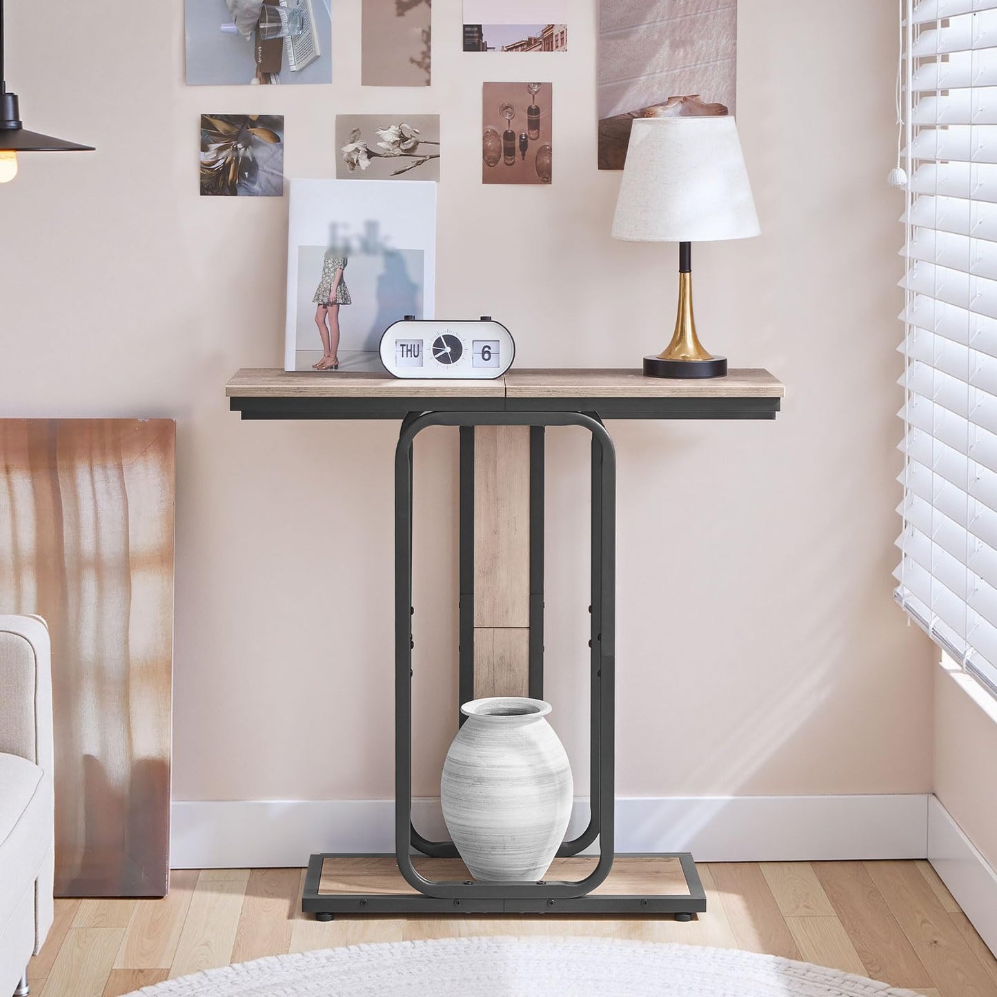 Compact hallway foyer table placed against a bedroom wall under picture frames holding a white clock.