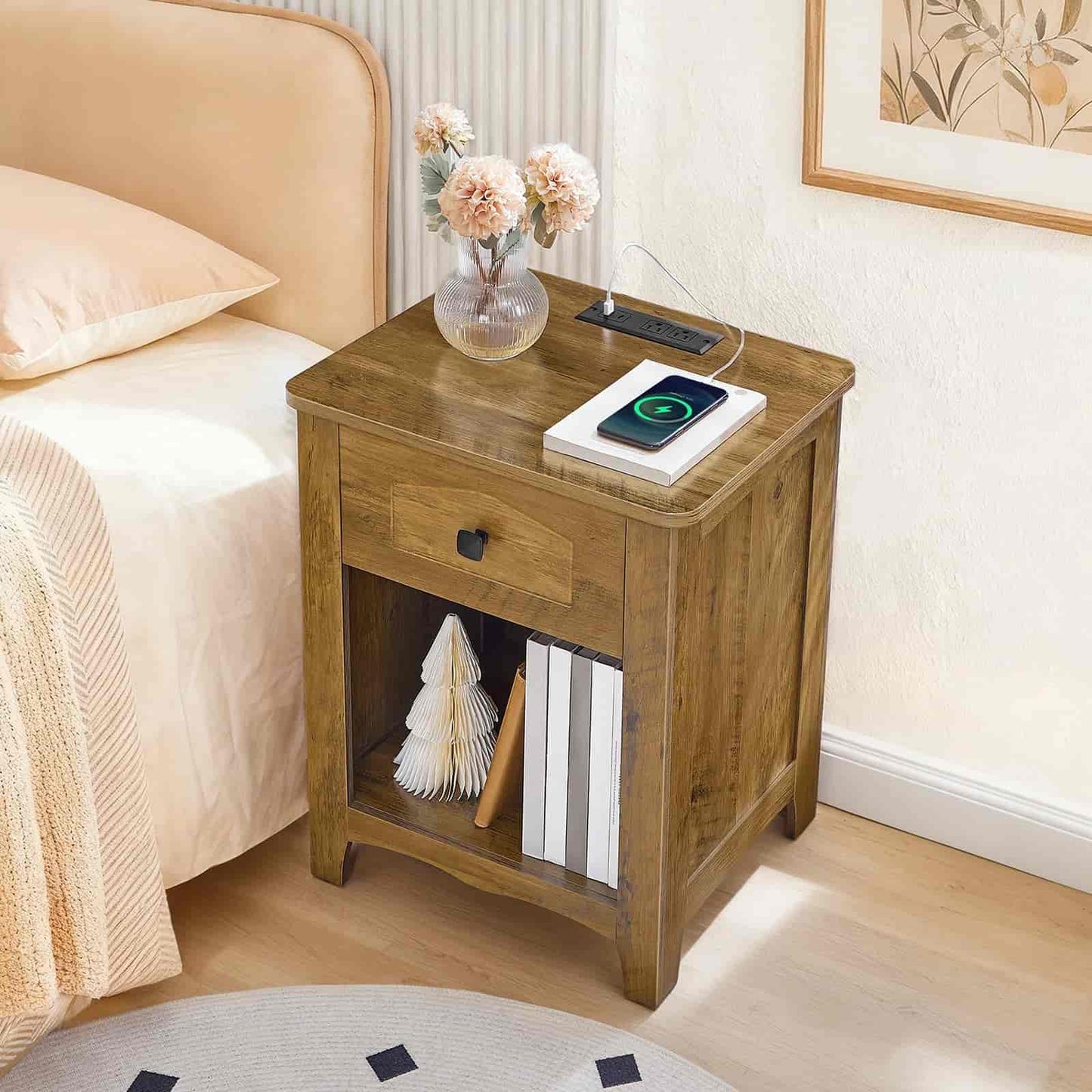 Wooden nightstand next to a bed with a phone, books, and a vase on top.