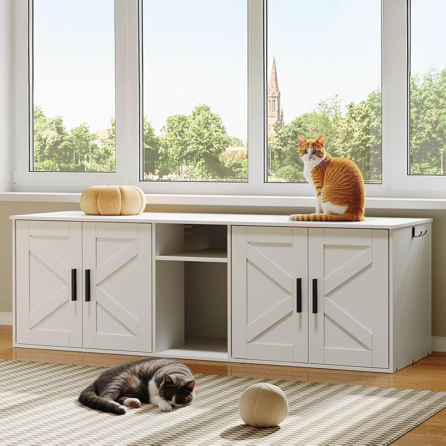 Two cats on a white entertainment console with large windows showing trees and a church spire.