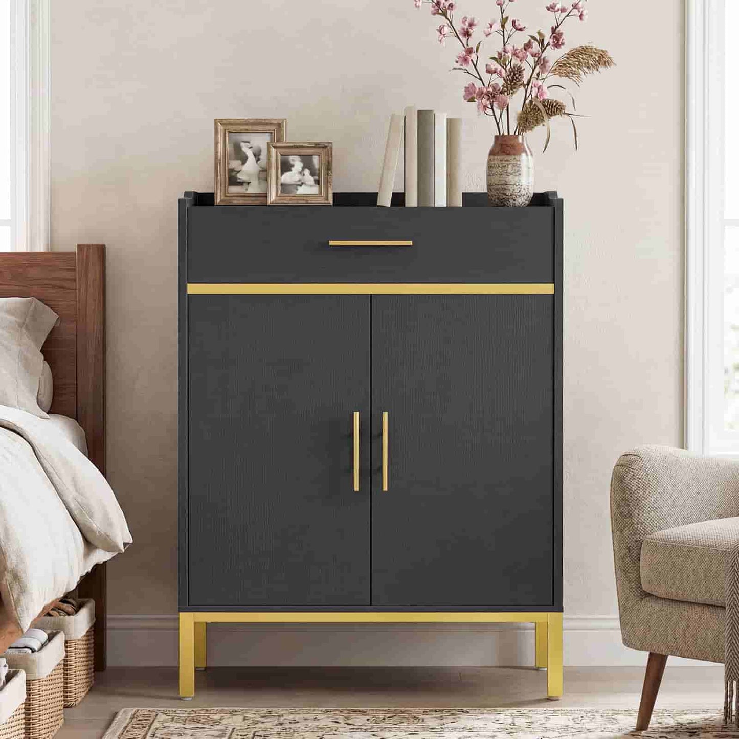 Elegant black accent storage cabinet with gold legs placed next to a bed and armchair in a modern home.