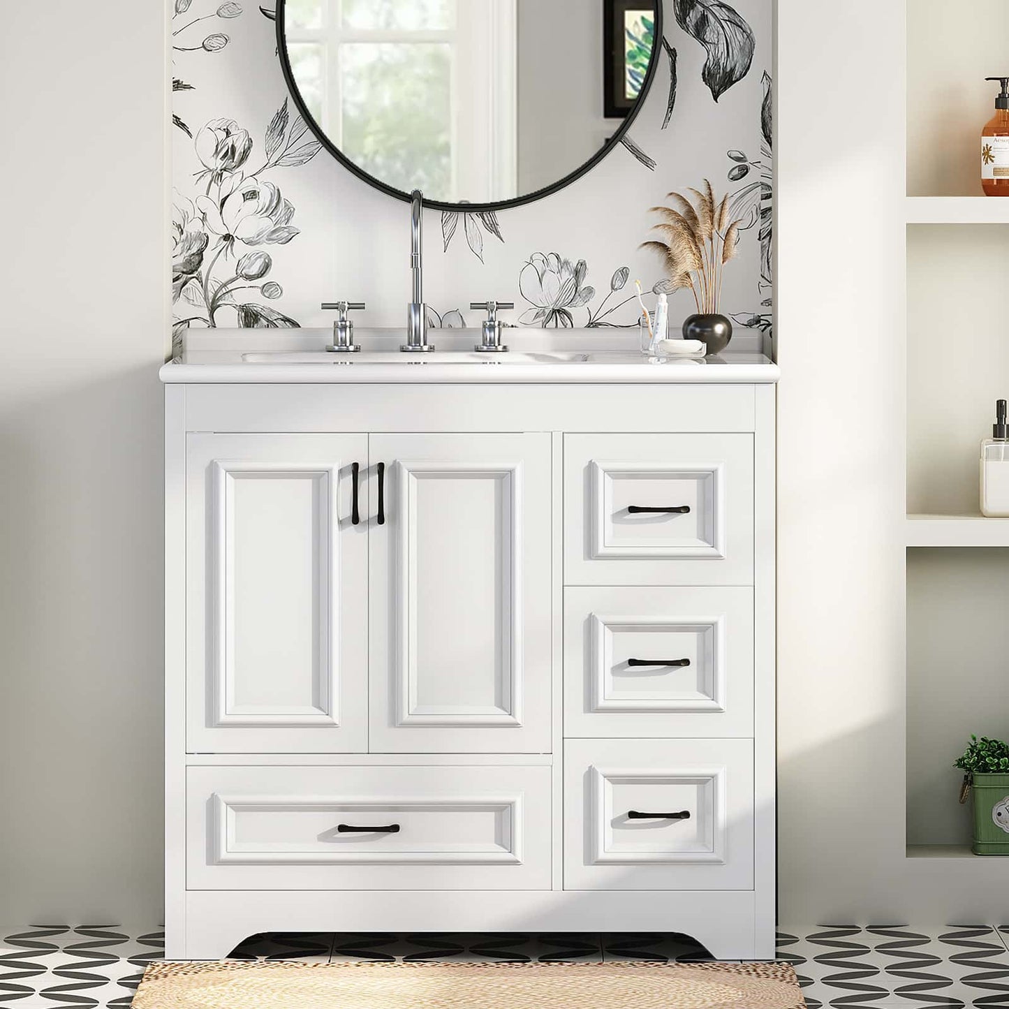 White bathroom vanity cabinet with an integrated white sink, chrome faucet, and black hardware, shown in a styled bathroom setting with floral wallpaper, a round mirror, and shelving.