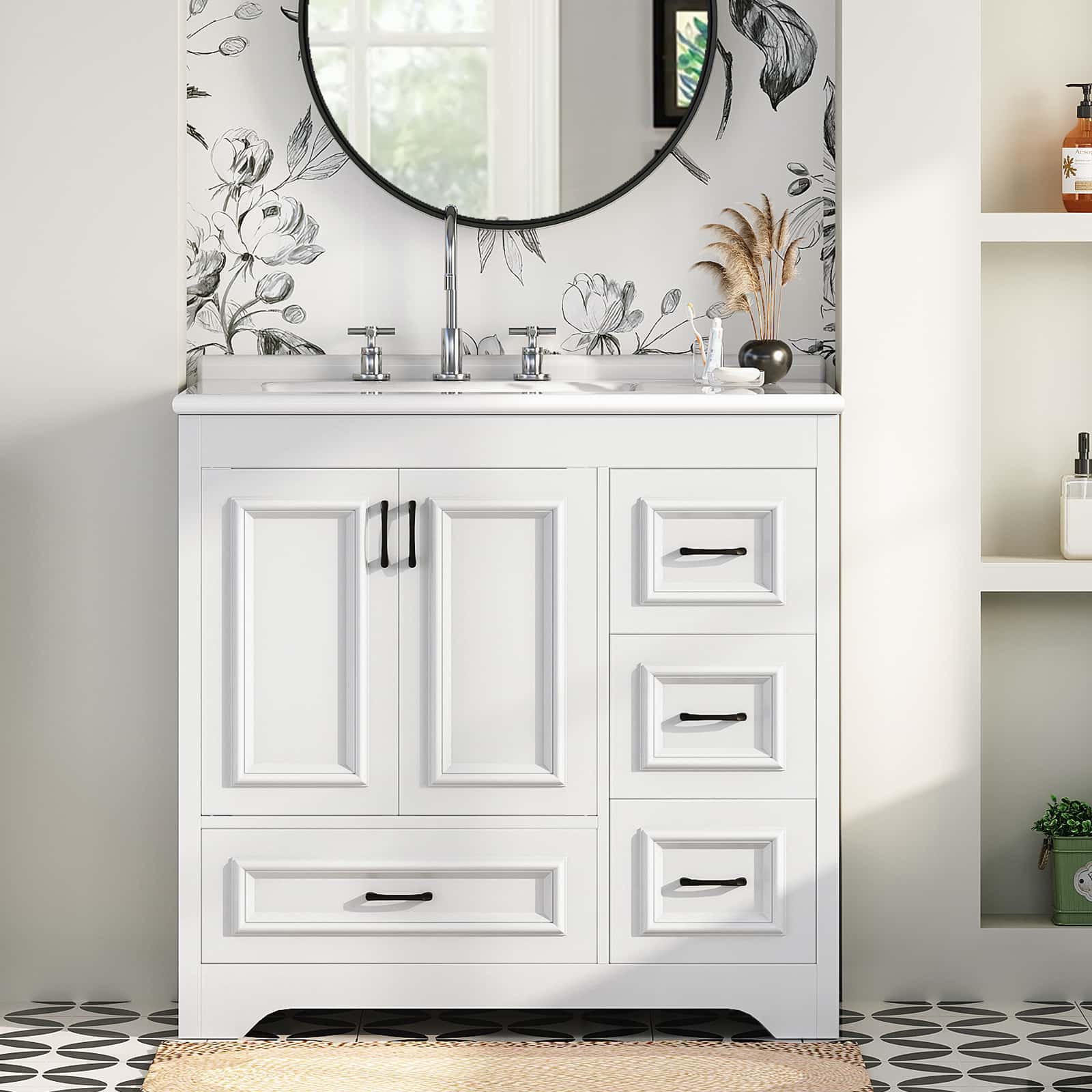 White bathroom vanity cabinet with an integrated white sink, chrome faucet, and black hardware, shown in a styled bathroom setting with floral wallpaper, a round mirror, and shelving.