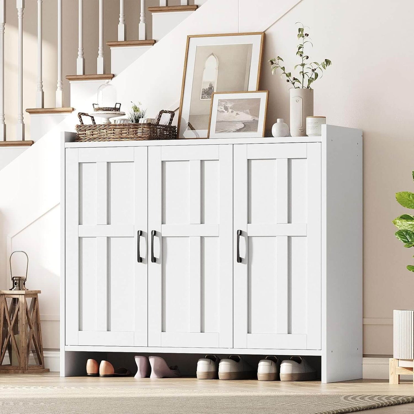 White storage cabinet with shoes underneath, placed in a room with a staircase and decorative items.