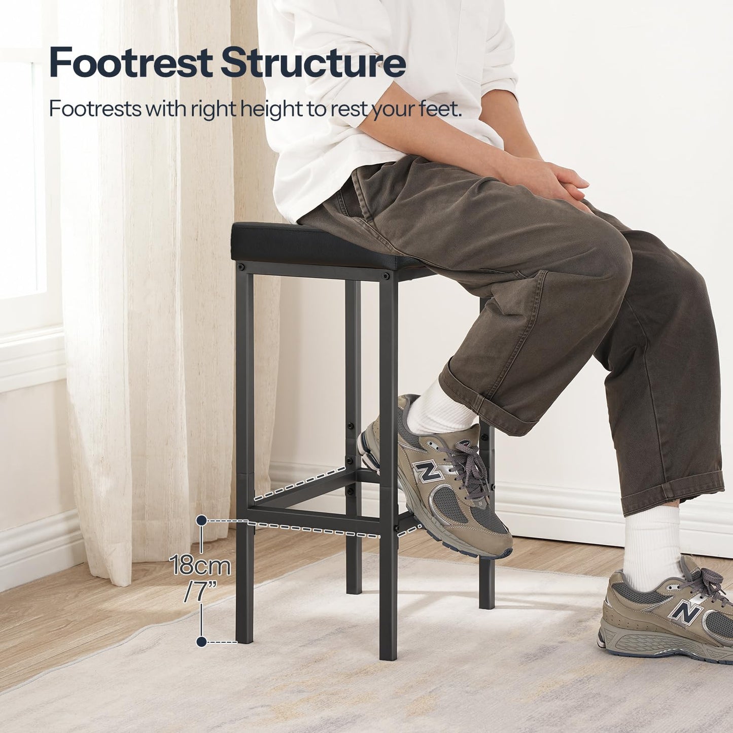 Side view of a person sitting on the black barstool demonstrating the ergonomic metal footrest structure.