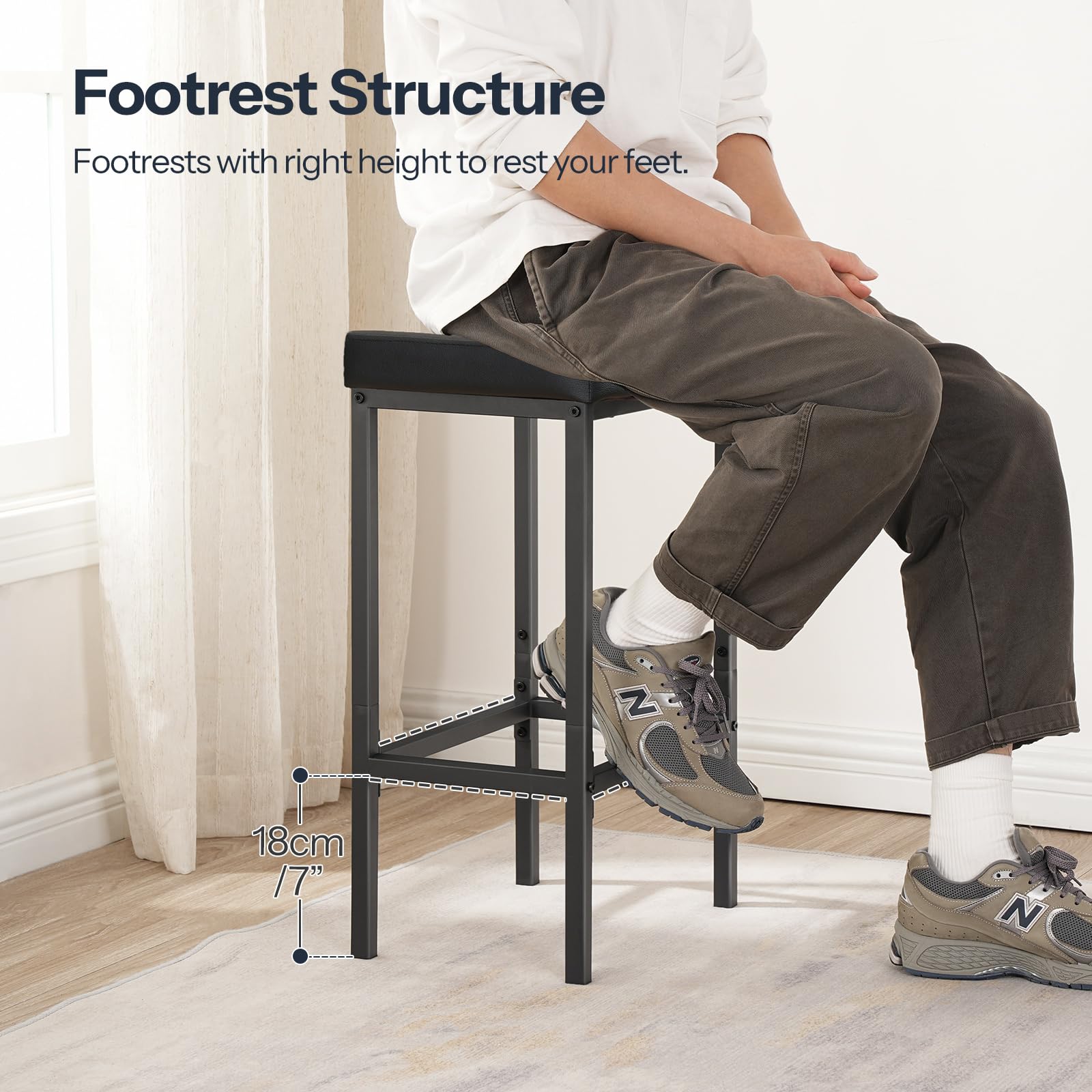 Side view of a person sitting on the black barstool demonstrating the ergonomic metal footrest structure.