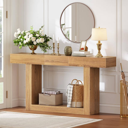 A light oak wood console table with a modern open design, styled in a bright entryway with a round mirror, a table lamp, a vase of white flowers, and storage baskets.