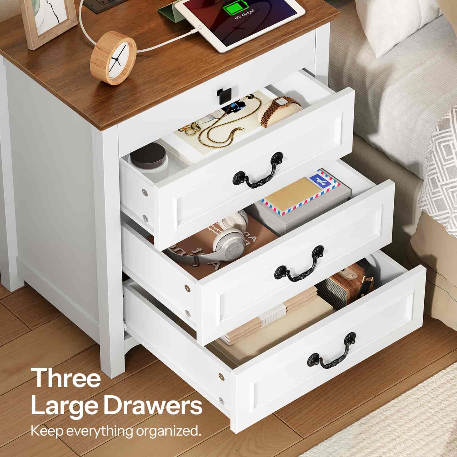 White nightstand with three large drawers, wooden top, and small clock on a wooden floor.