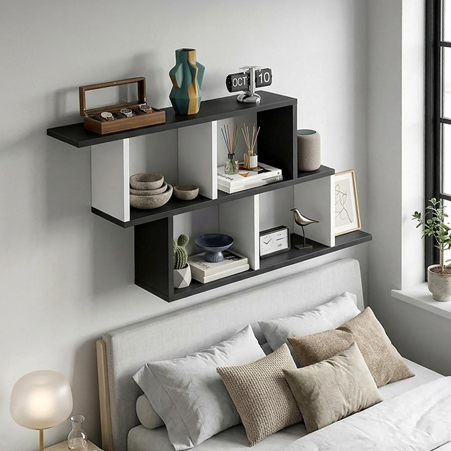 Black and white wall-mounted floating bookshelf installed above a bed in a modern bedroom.