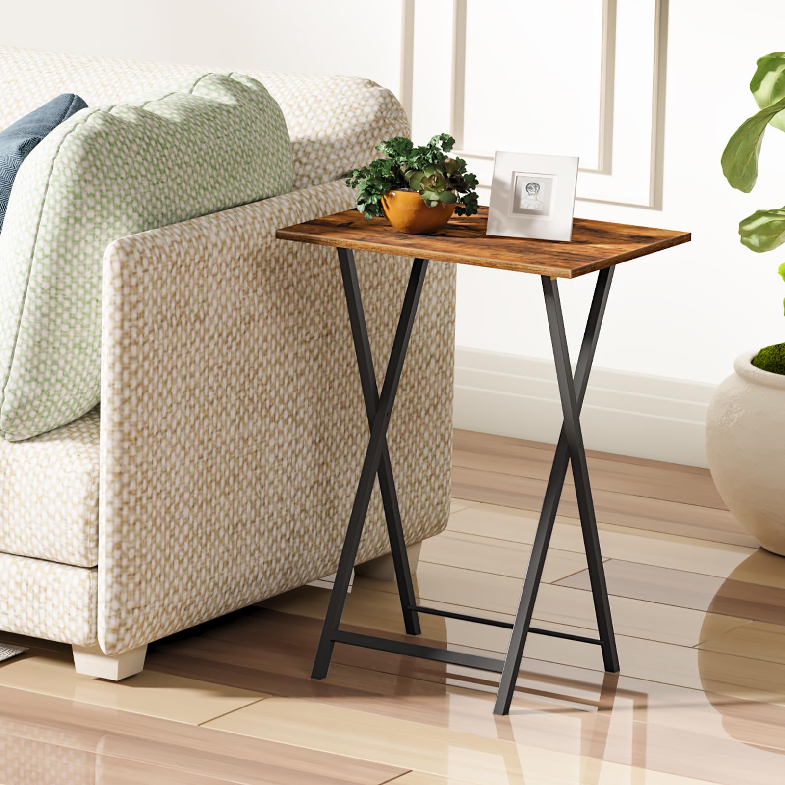 Rustic brown foldable TV tray table standing neatly next to a living room sofa holding plants.
