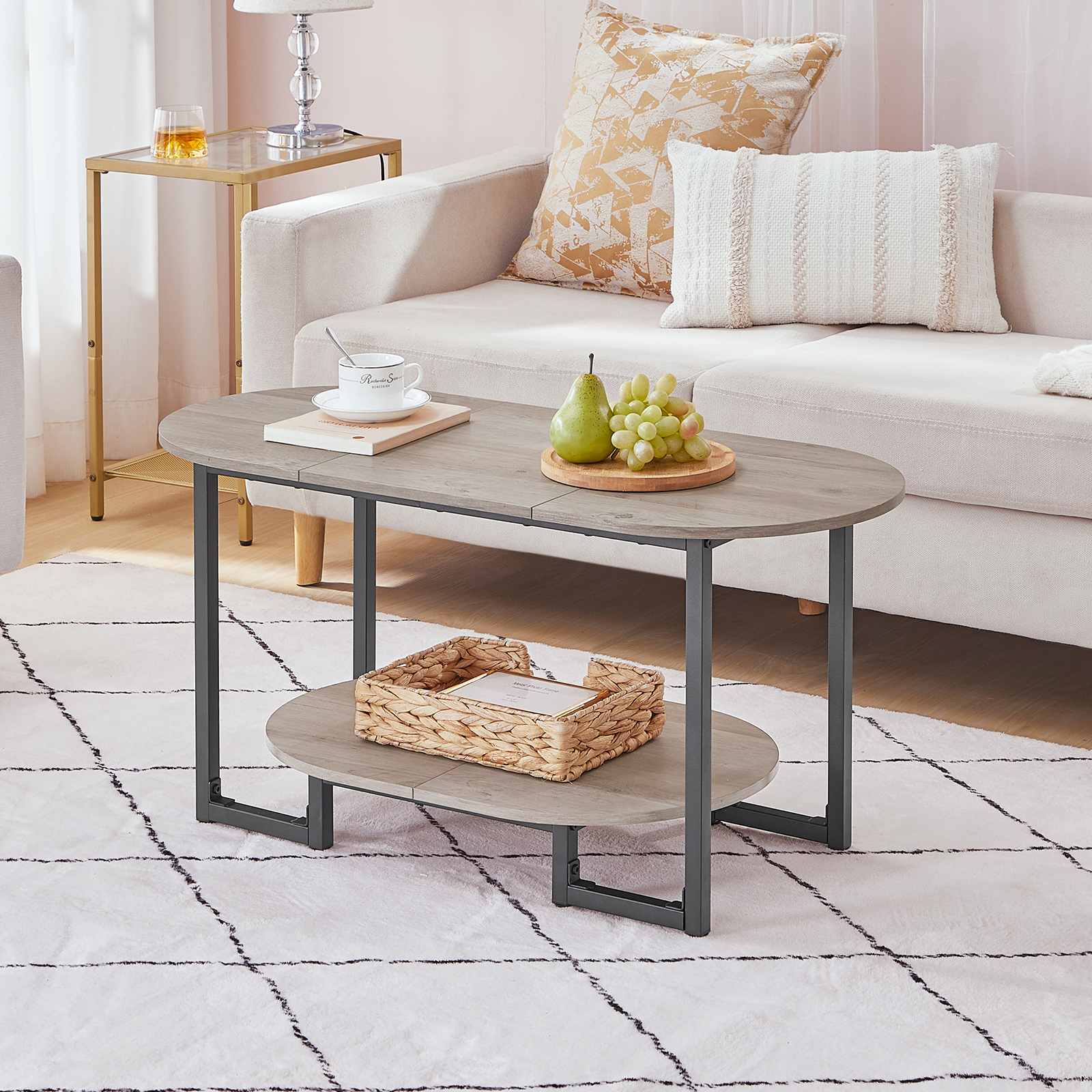 Modern greige oval coffee table styled on a geometric rug next to a white fabric couch.