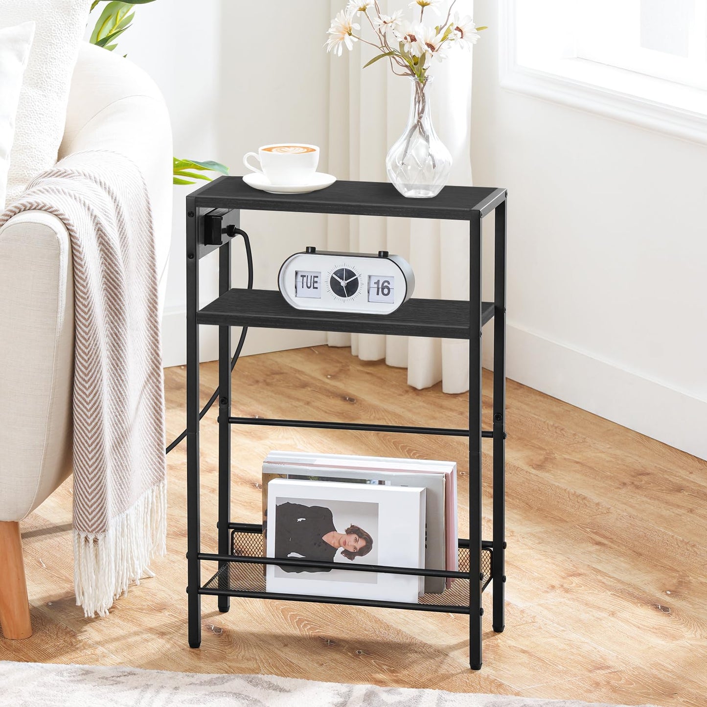 HOOBRO skinny black end table with a side charging station standing next to a cream couch holding an alarm clock.