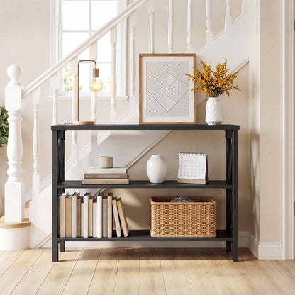 Slim black industrial console table placed by a wooden staircase hallway, decorated with a lamp, picture frame, and books.