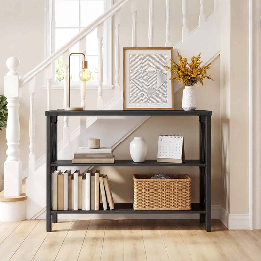 Slim black industrial console table placed by a wooden staircase hallway, decorated with a lamp, picture frame, and books.