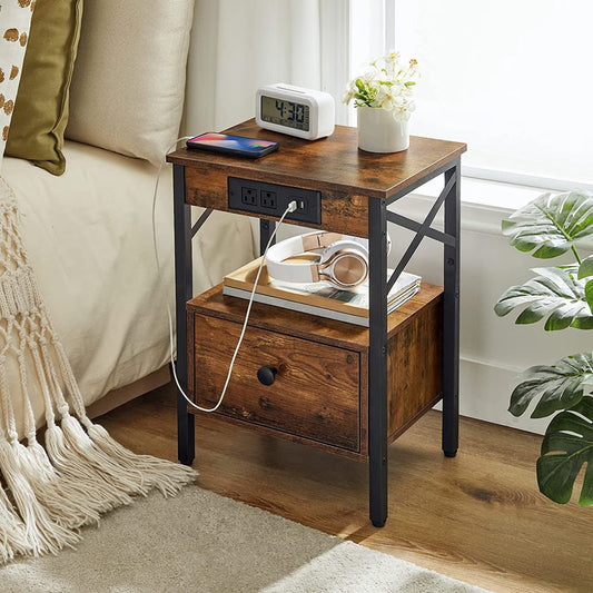 Rustic brown industrial nightstand with charging station styled next to a bed holding a phone, clock, and headphones.