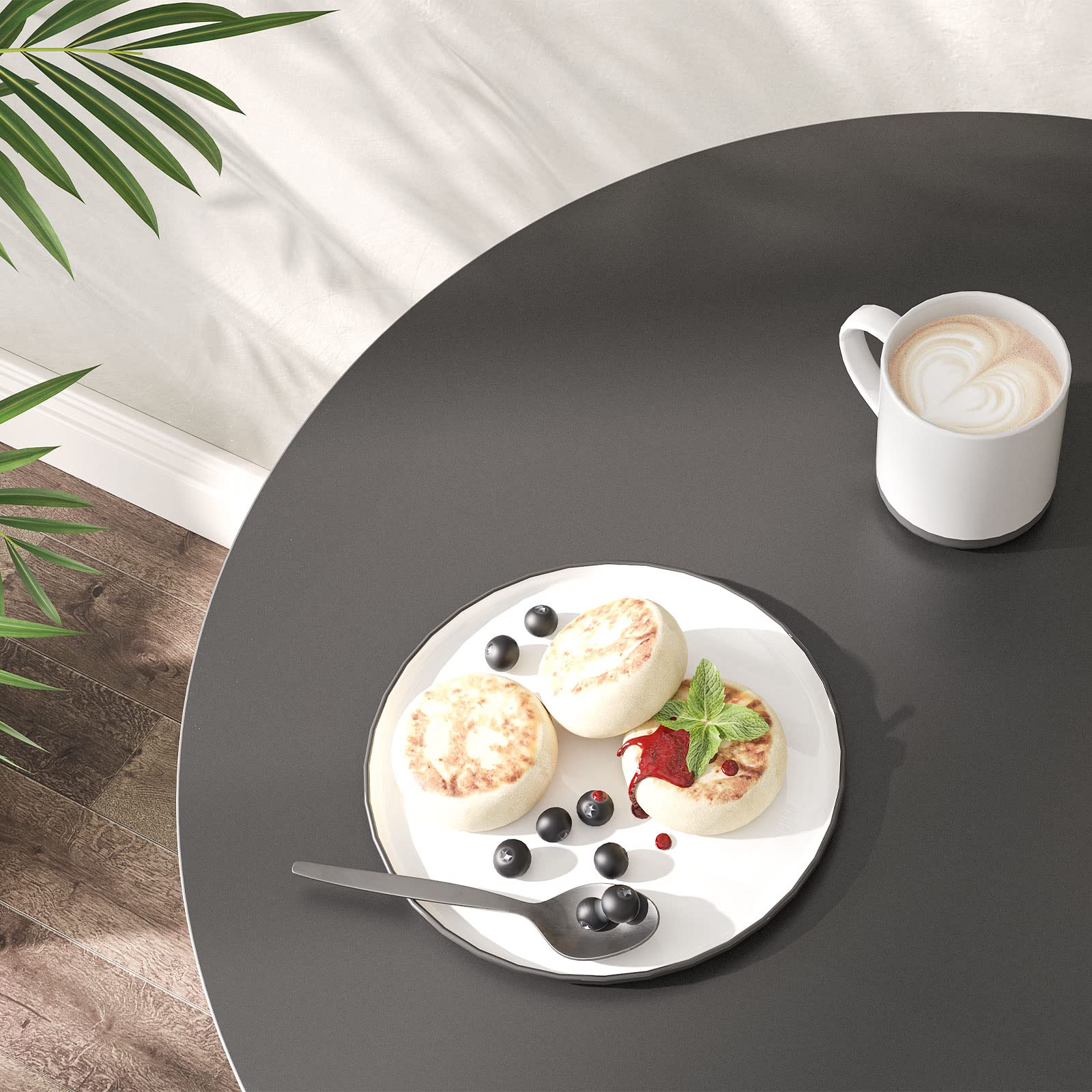 Close up of the sleek matte black round tabletop holding a white plate of cake and a ceramic coffee mug.