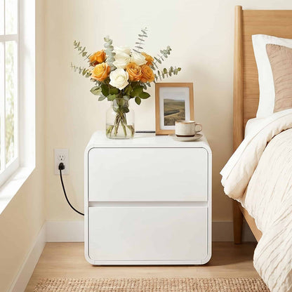White nightstand with a vase of flowers and a mug next to a bed.