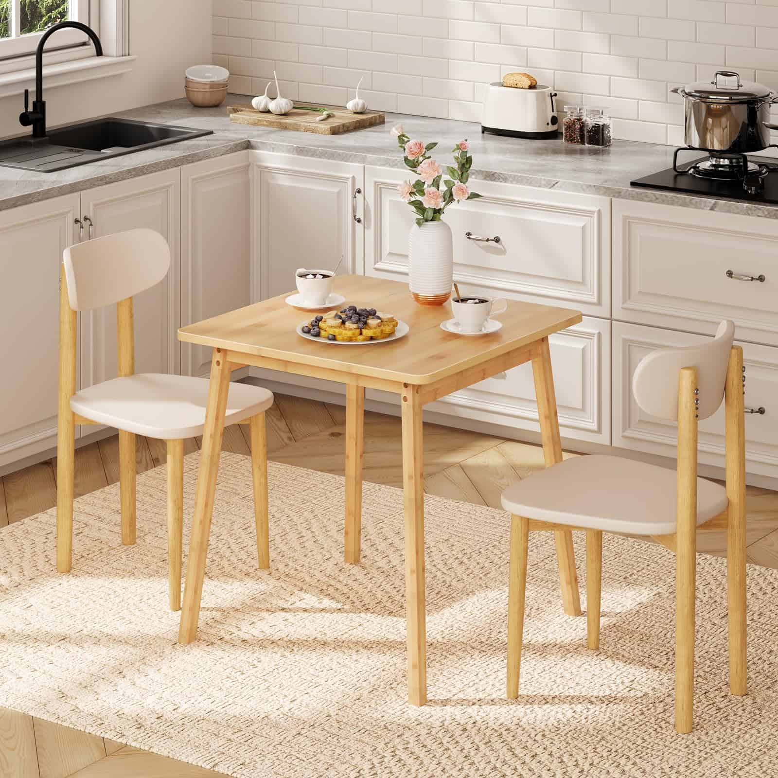 Modern natural bamboo square dining table for two set up with plates and chairs in a bright, white kitchen.