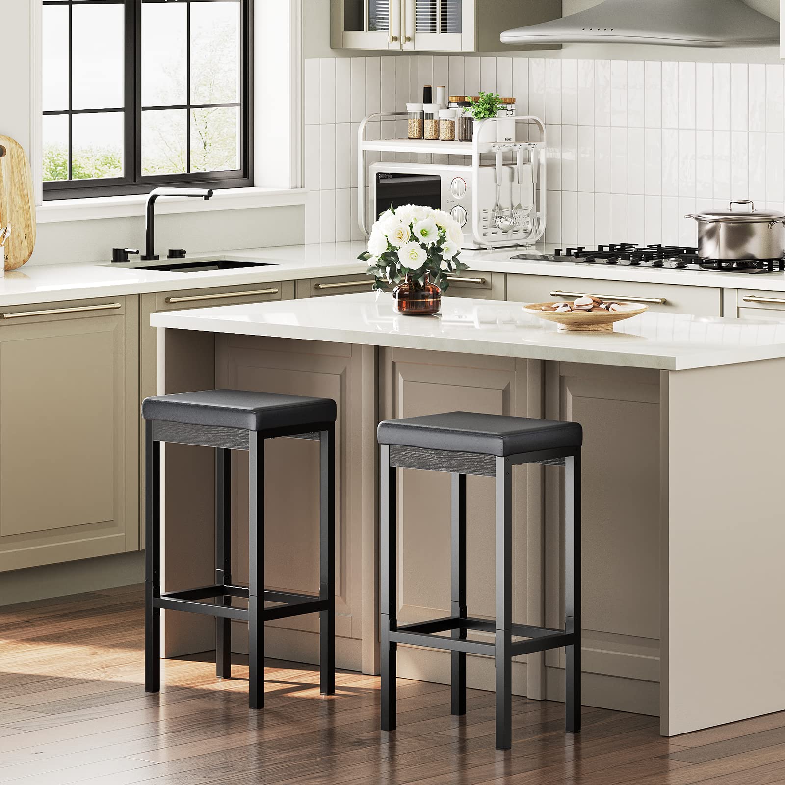 Set of 2 modern black bar stools with thick padded seats placed next to a white kitchen island.