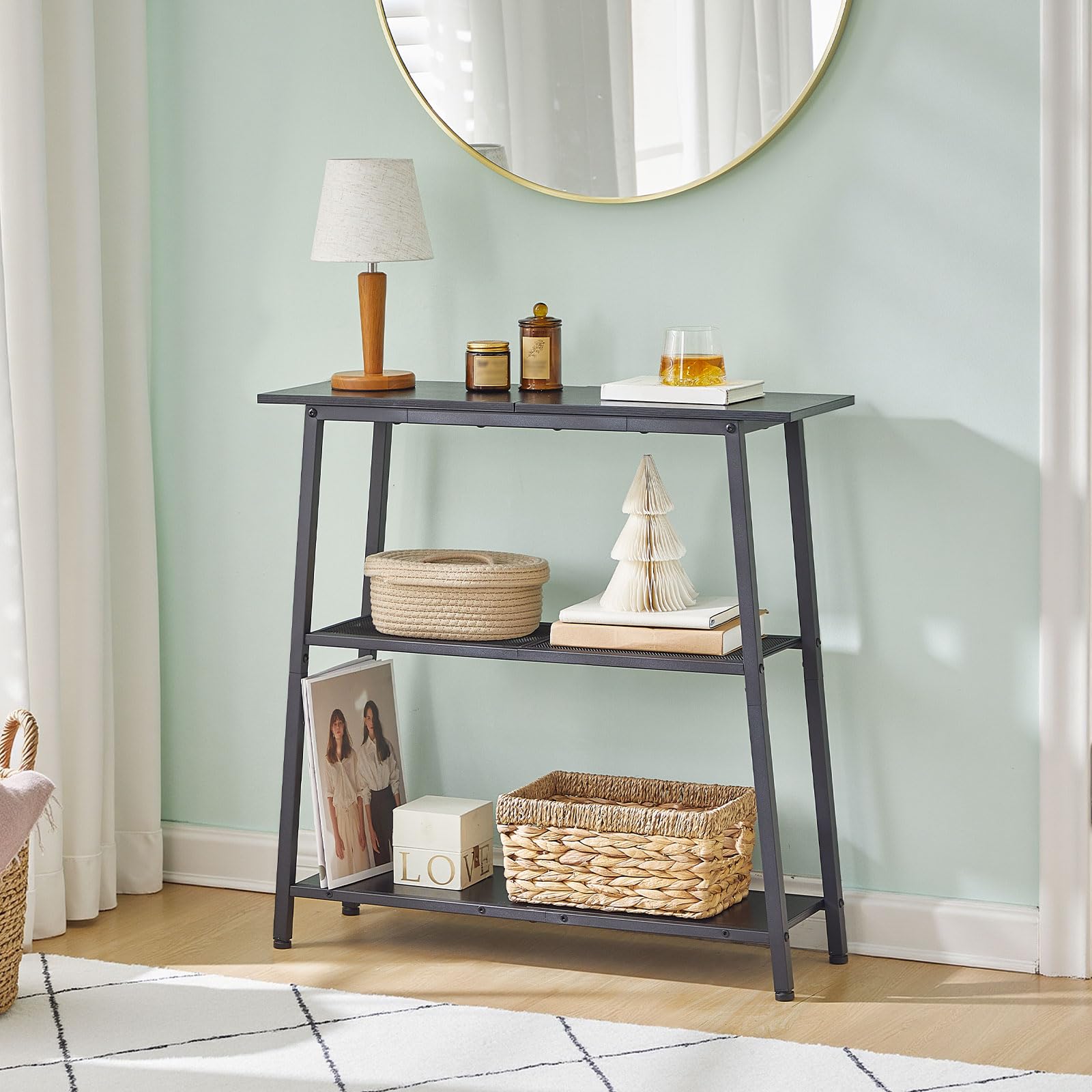 Modern black foyer table placed against a pastel green entryway wall underneath an elegant hanging circular mirror.