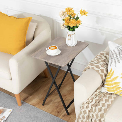 Narrow rustic folding couch side table styled with a teacup and flower vase next to a beige armchair.
