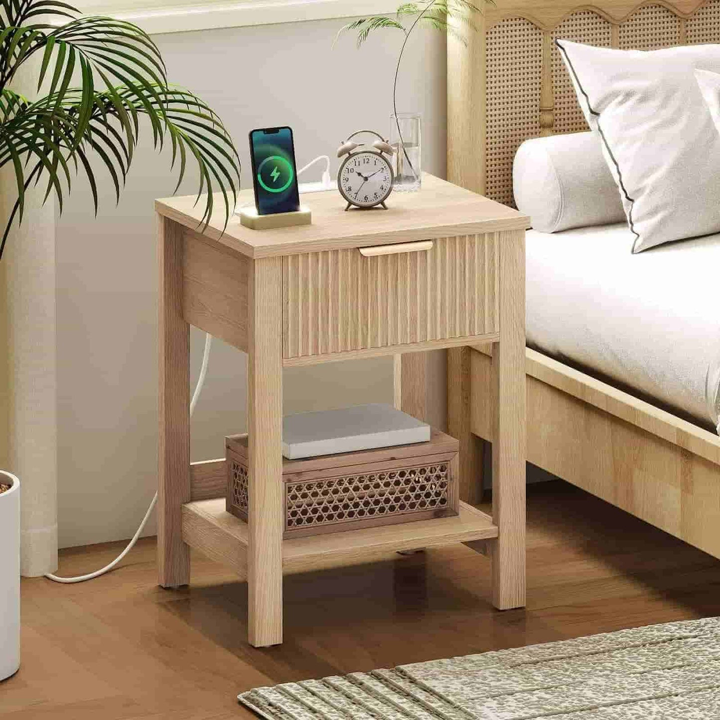 Wooden nightstand with phone, clock, and laptop next to a bed