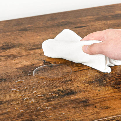 Person applying a clear liquid to a wooden surface with a white cloth.