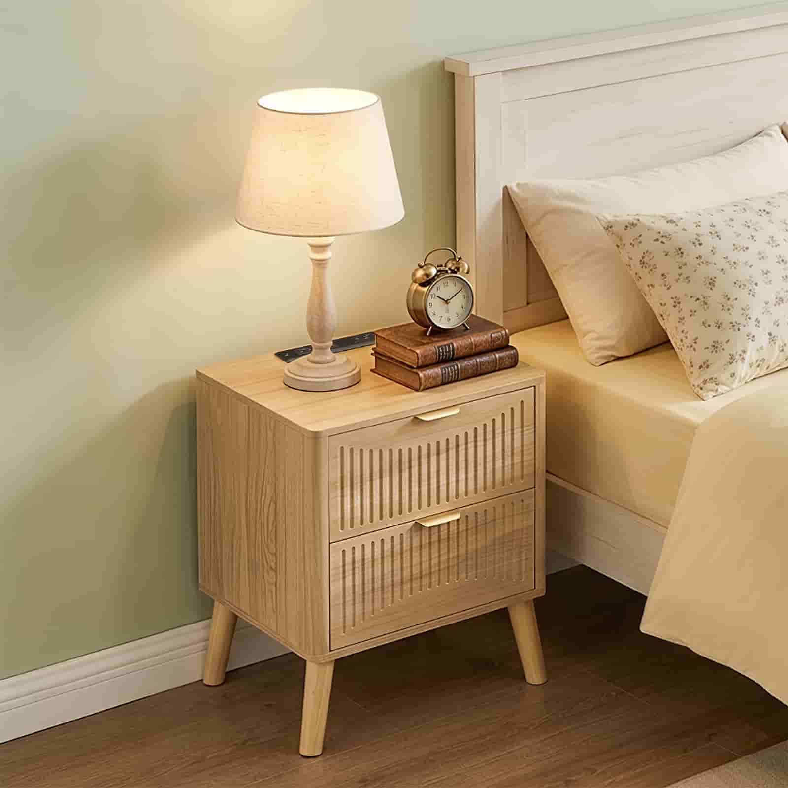 Boho style wood nightstand with 2 drawers and a warm table lamp placed next to a bed in a cozy bedroom.