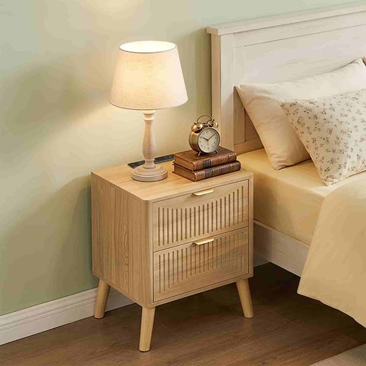 Boho style wood nightstand with 2 drawers and a warm table lamp placed next to a bed in a cozy bedroom.