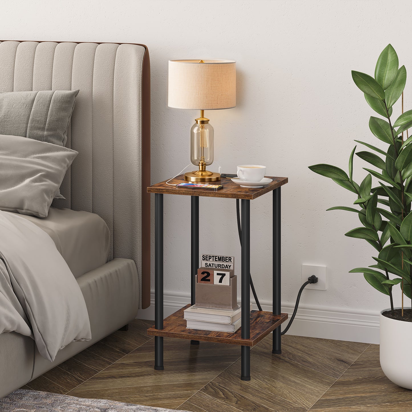 Rustic brown bedside table holding a gold table lamp and books placed next to a modern grey fabric bed.