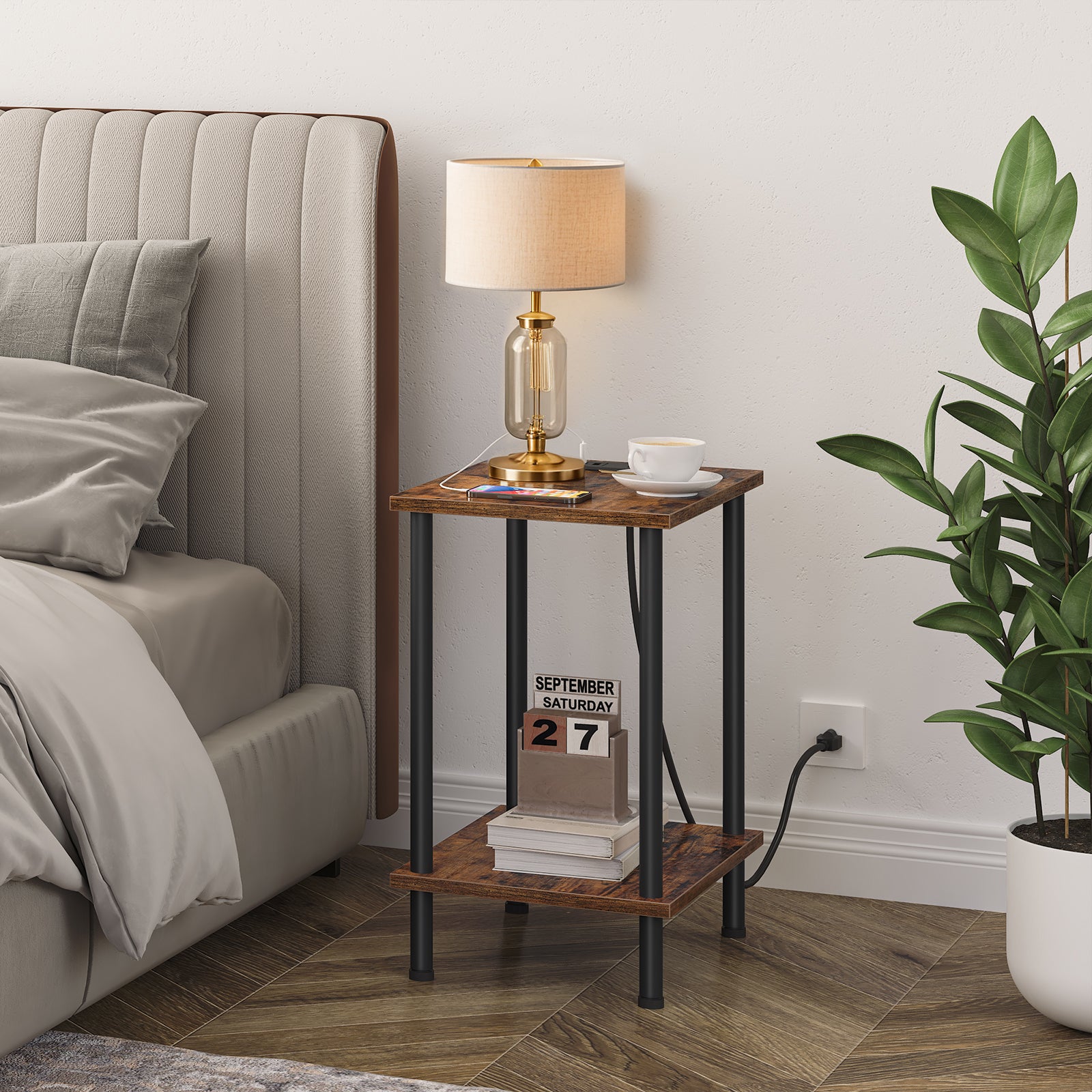 Rustic brown bedside table holding a gold table lamp and books placed next to a modern grey fabric bed.