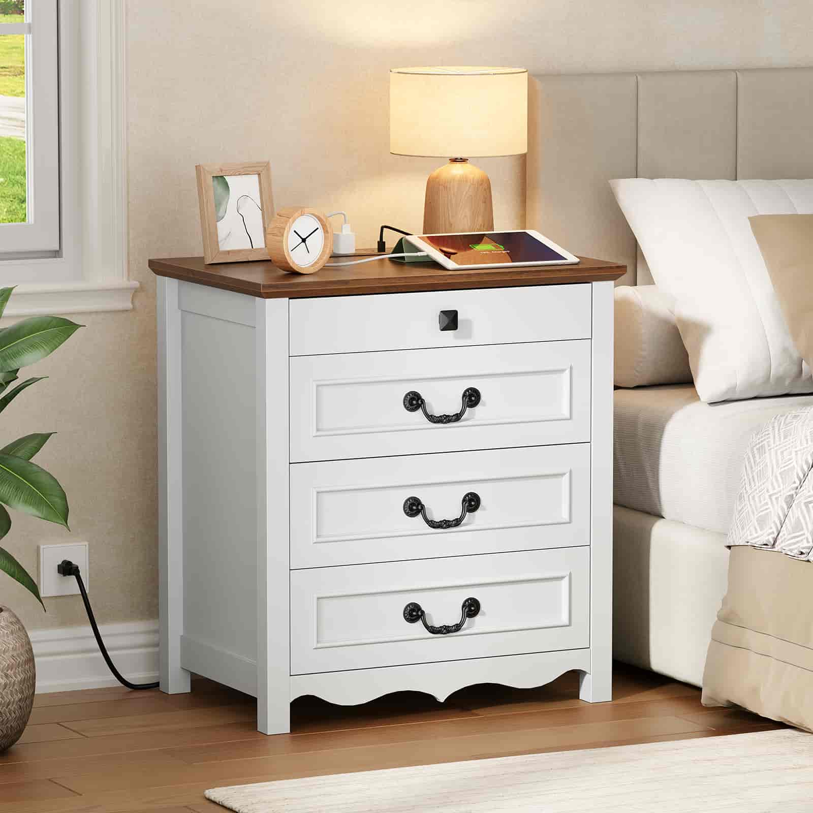 Cozy bedroom scene showing the white charging nightstand with a warm lamp next to a neatly made bed.