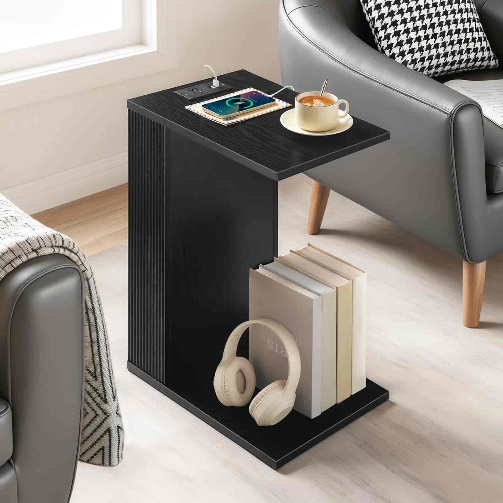Black side table with books, headphones, and a cup in a living room setting.