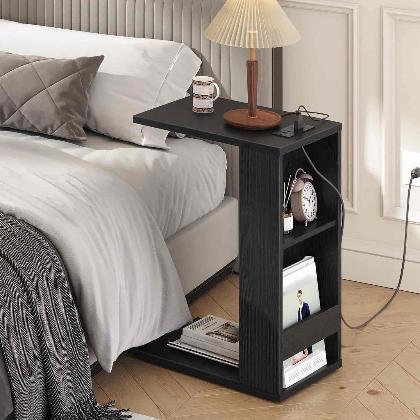 Black side table with lamp, clock, and books next to a bed in a bedroom.