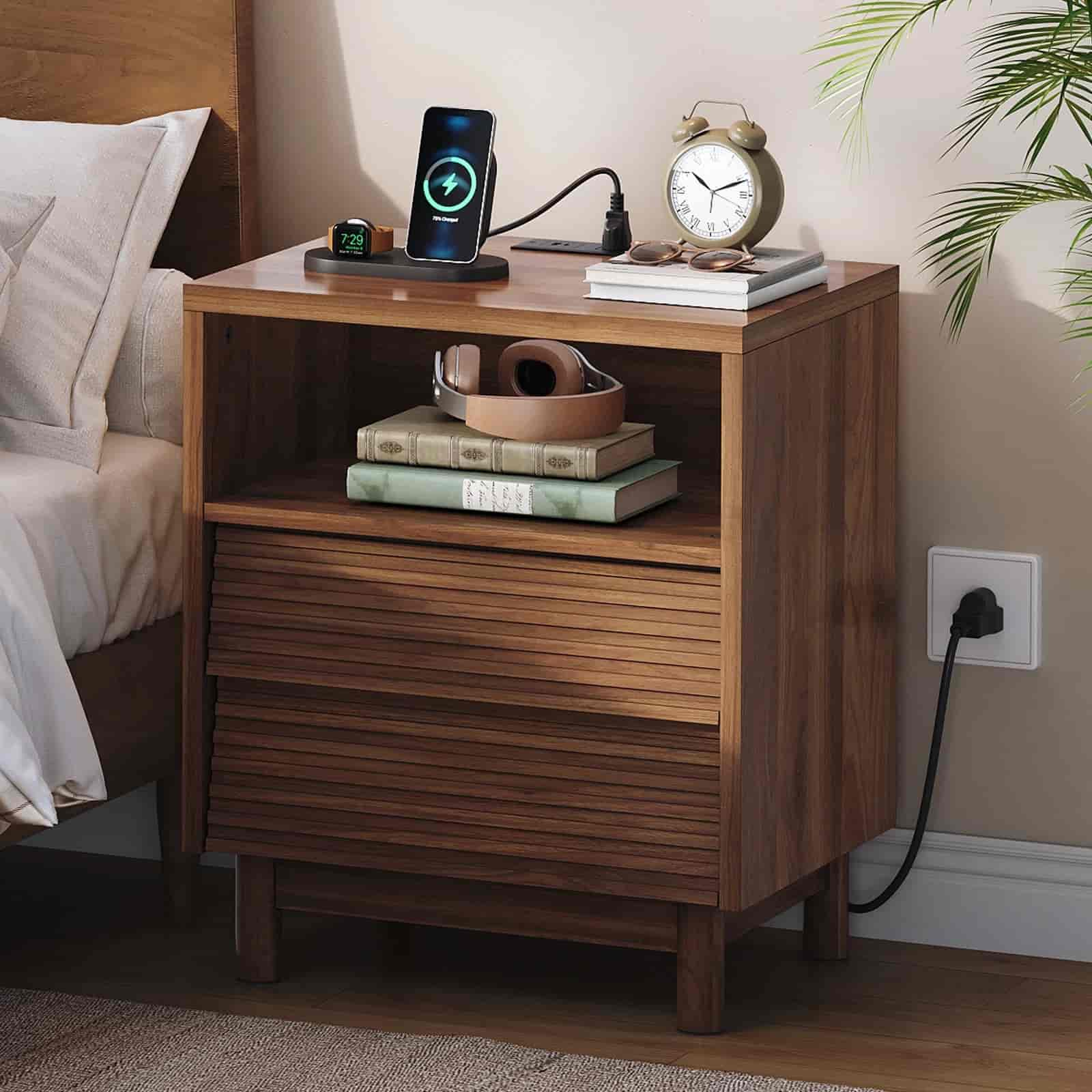 Wooden nightstand with electronic devices and books in a bedroom setting