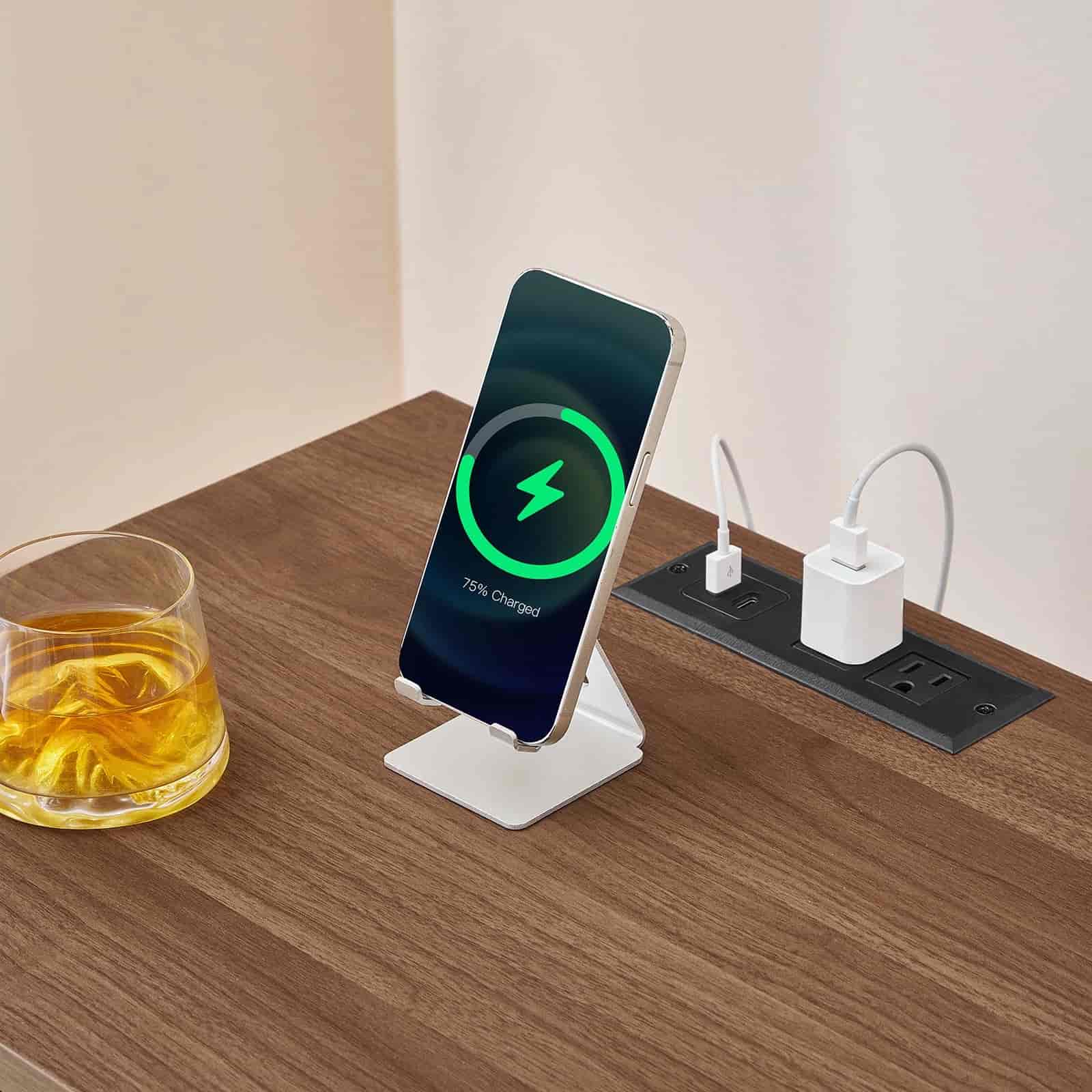 Wireless phone charger on a wooden desk with a glass of juice and a power strip.