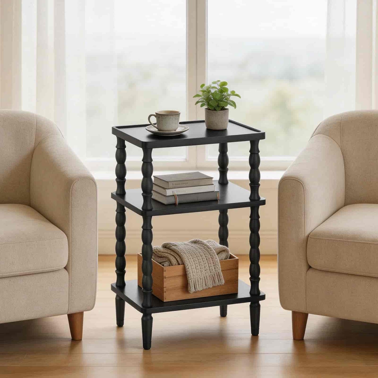 Black side table with decorative items between two beige armchairs in a room with large windows.