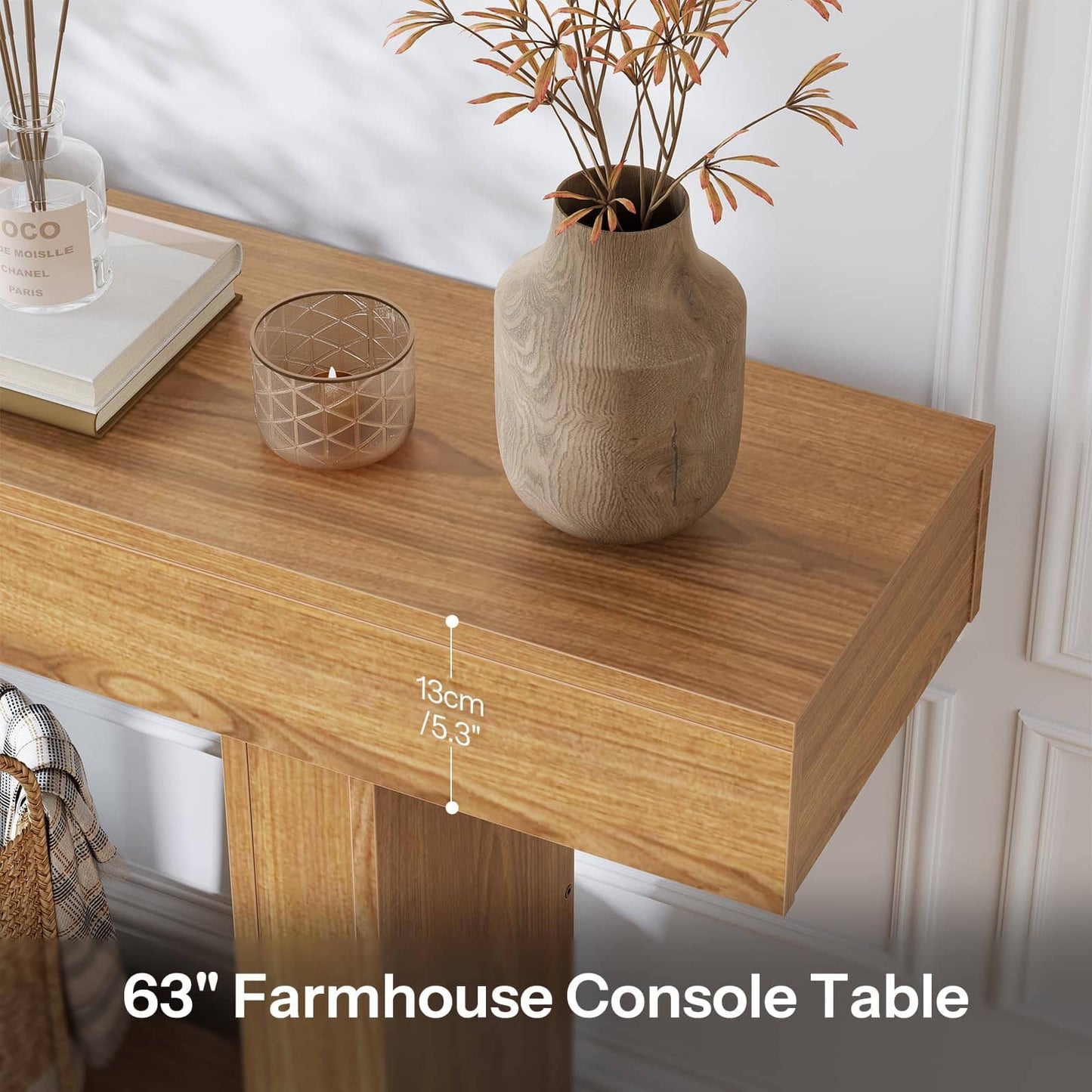 A 63-inch farmhouse console table in a warm medium brown wood finish, styled with a textured beige vase, a glass candle holder, and books on top. A white wall paneling background is visible, and a text overlay indicates the table height is 13cm (5.