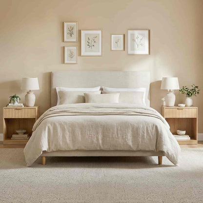 Neatly made bed with beige bedding in a bedroom setting with matching nightstands and decor.