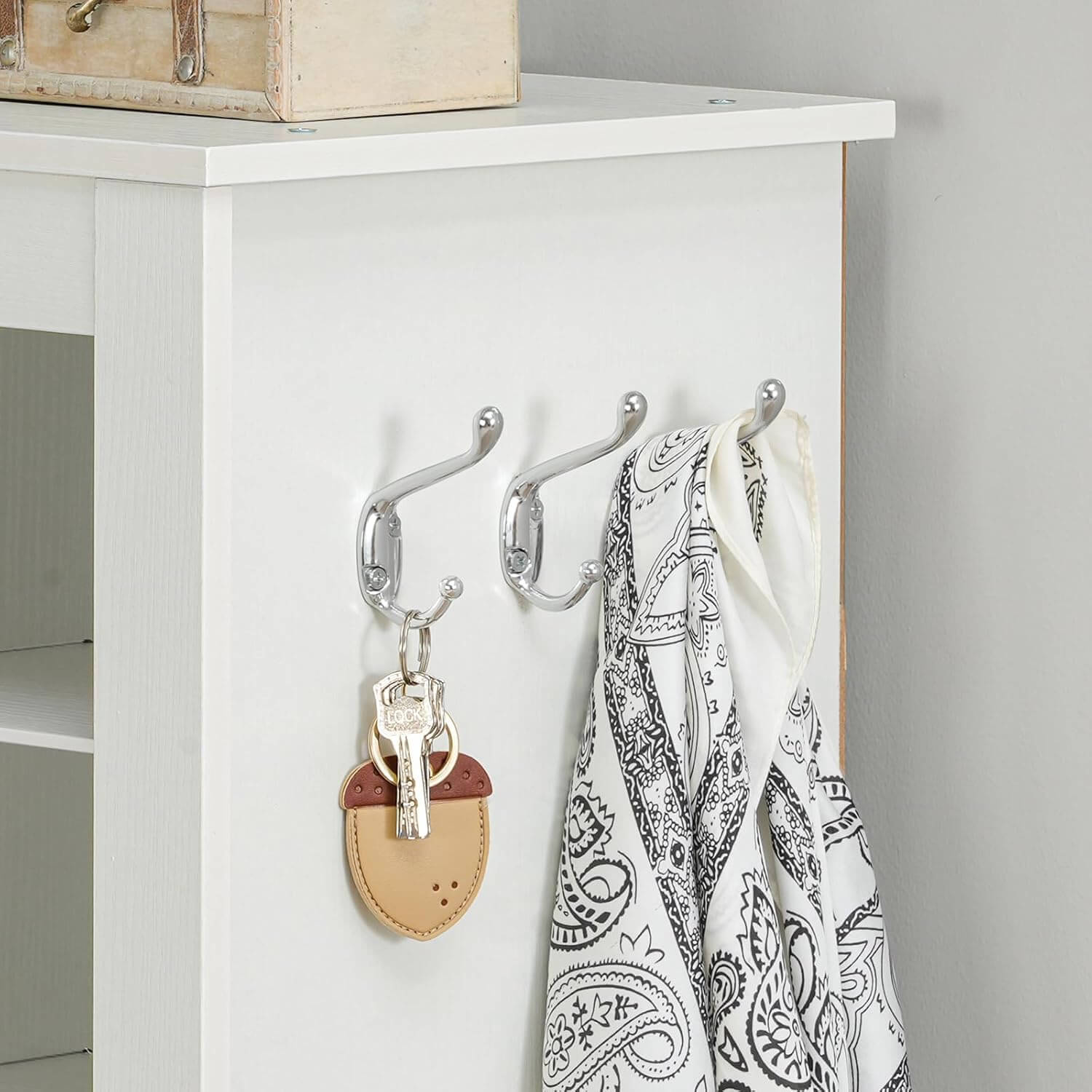 Close-up of 3 sturdy side hanging metal hooks on the white cabinet holding bags and scarves.