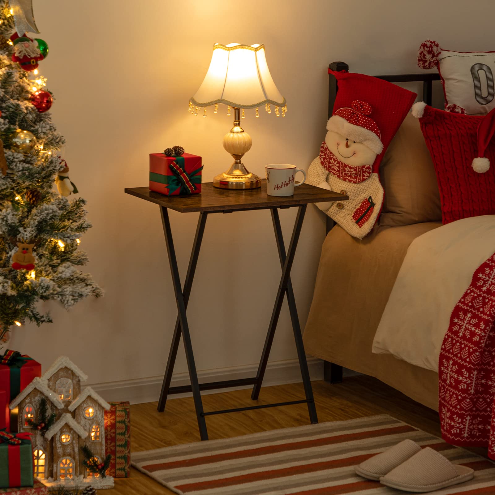 Foldable table used as a temporary bedside nightstand holding a lamp next to a decorated bed.