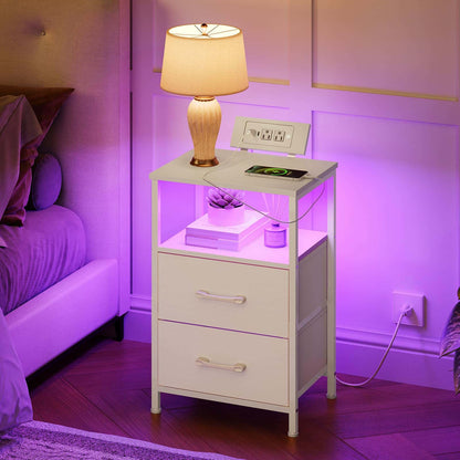 White nightstand with lamp and electronic devices in a bedroom setting