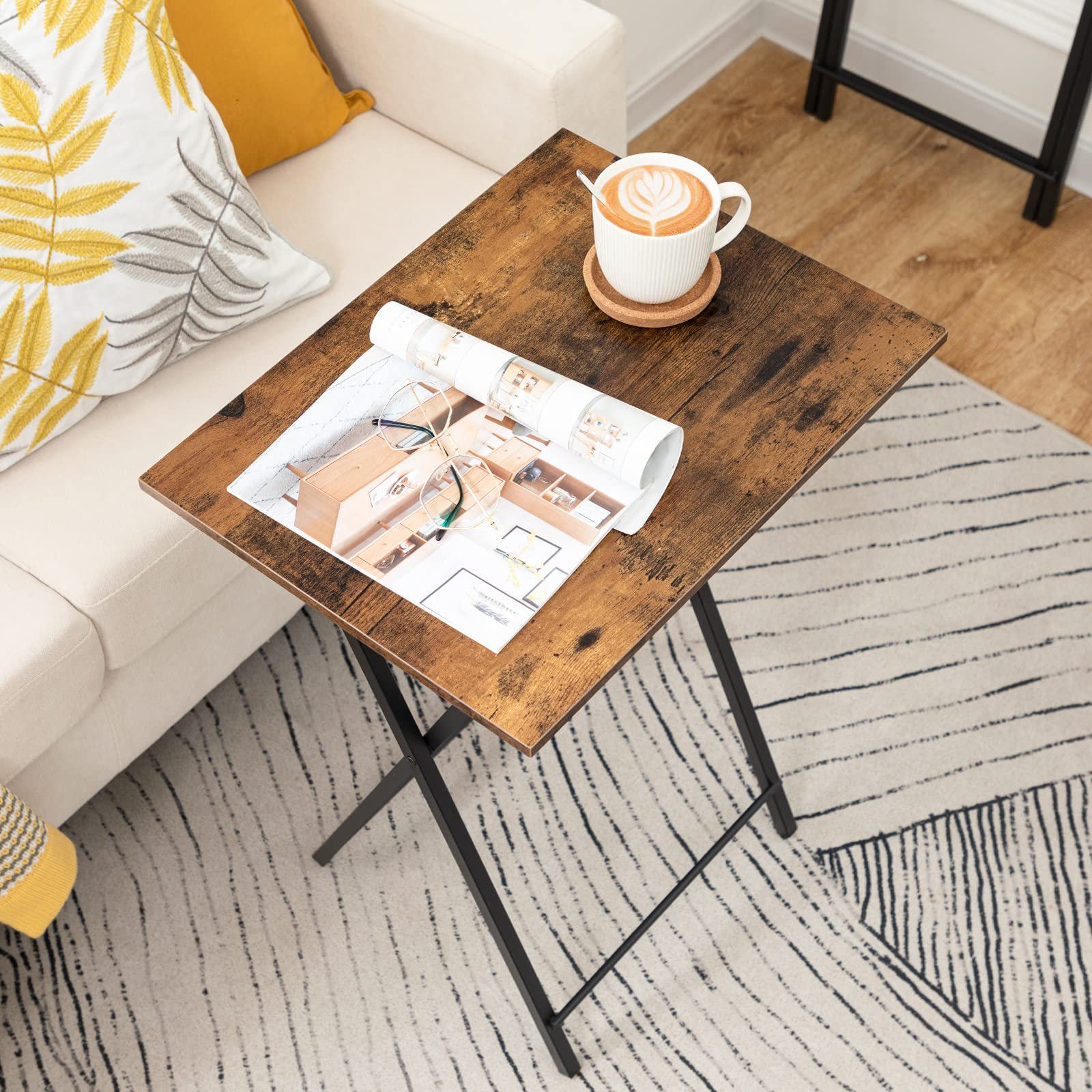 Wooden couch side snack table holding a coffee cup and an open magazine in a living room.